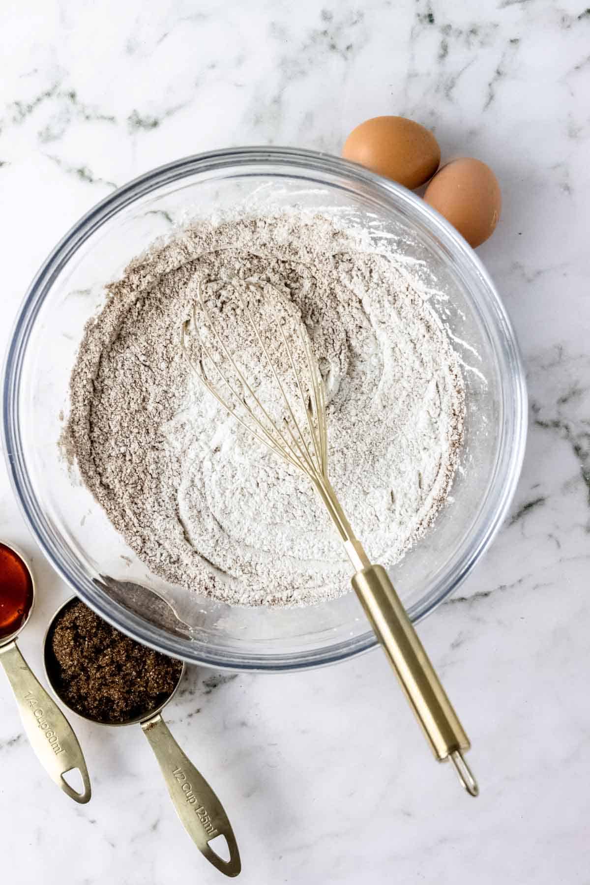 Dry gingerbread ingredients combined in a glass bowl with a whisk.
