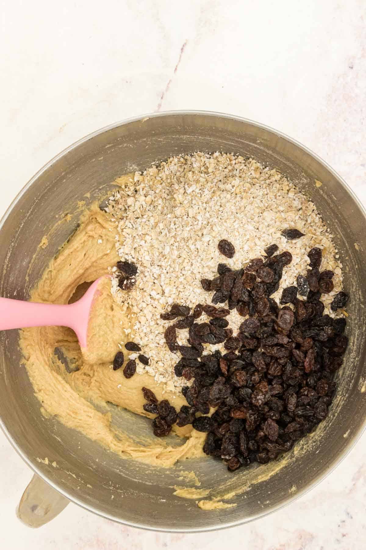 Oats and raisins are added into a bowl of cookie dough.