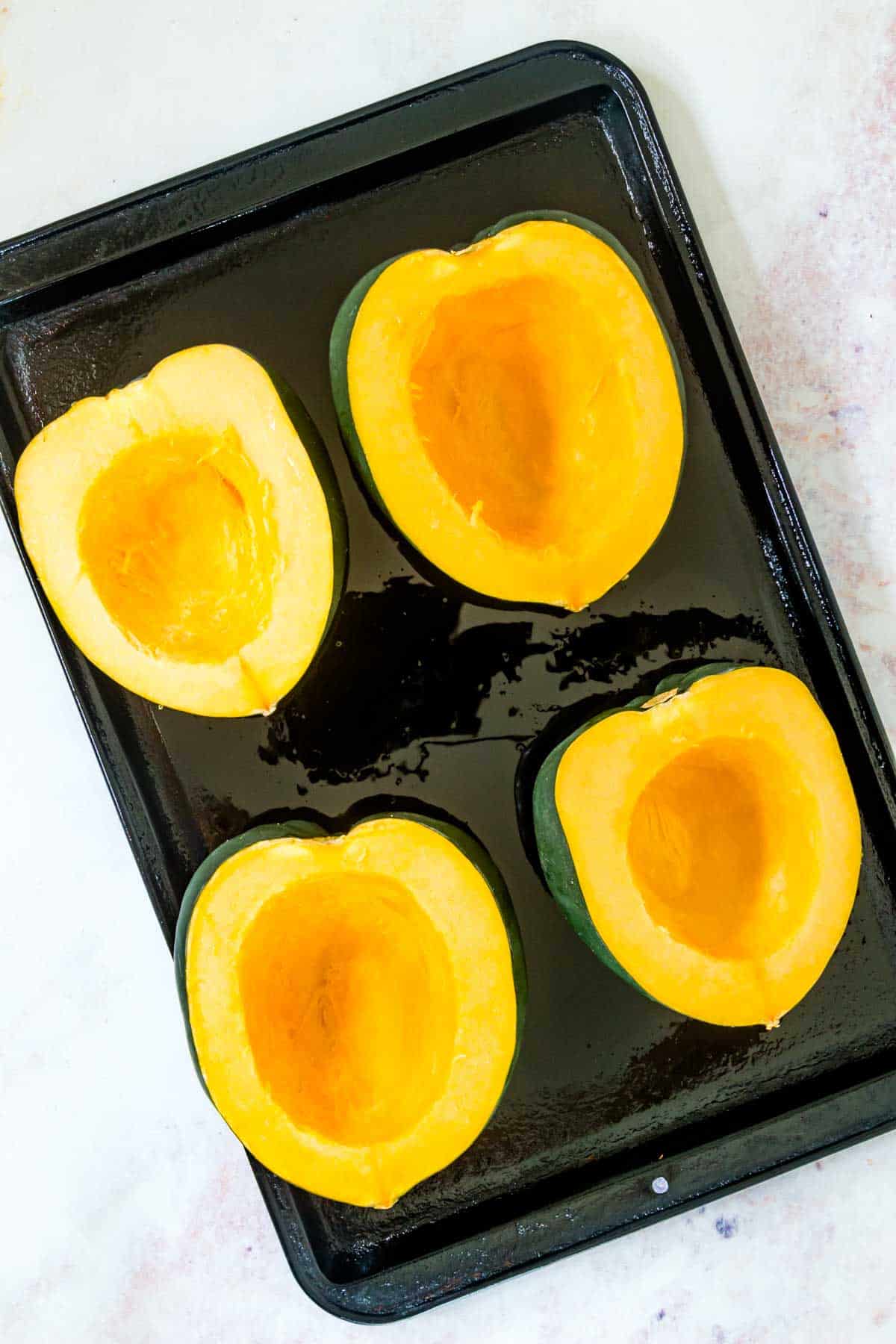 Four acorn squash halves cut side up on a baking sheet with the seeds scooped out.