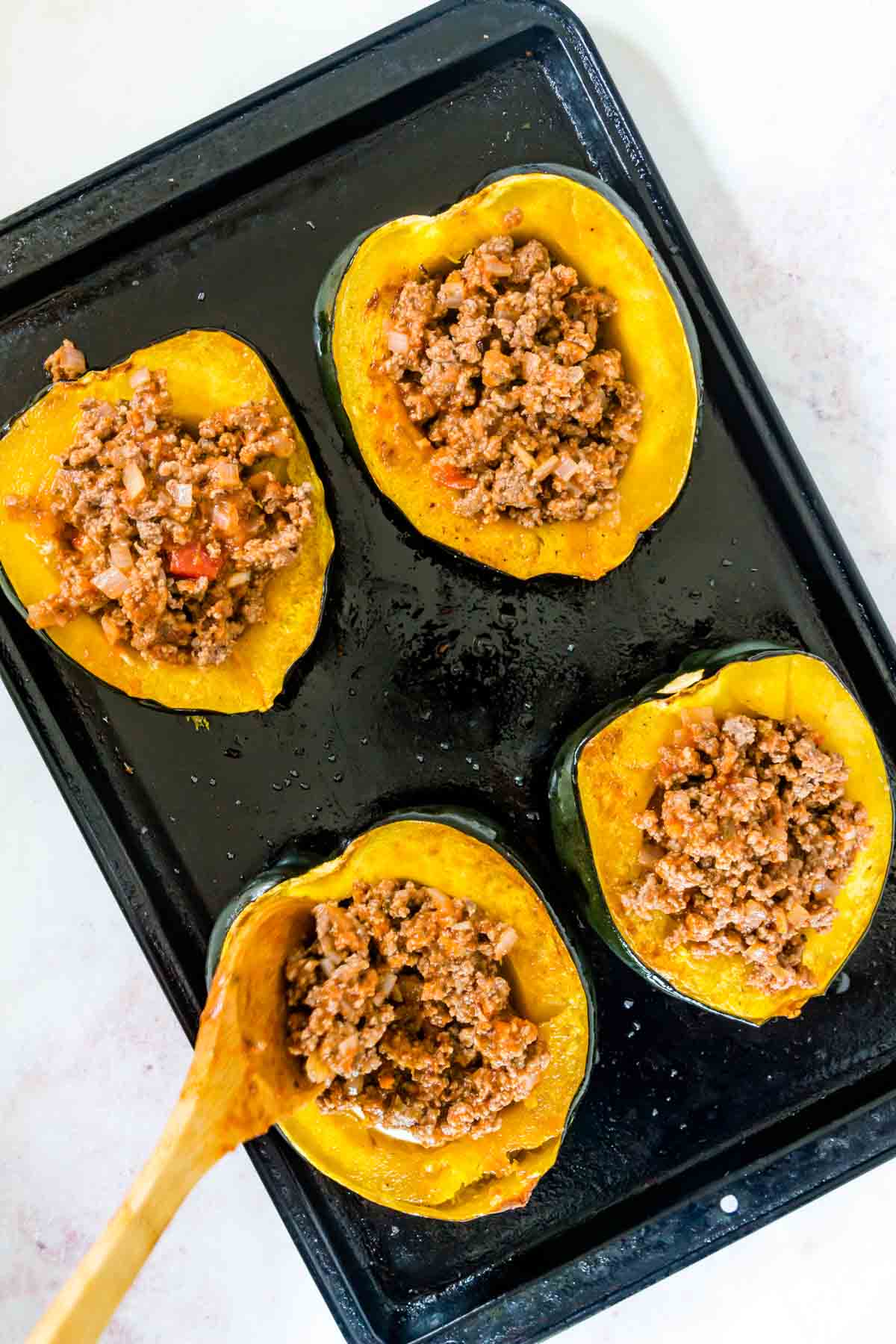 Italian meat sauce being spooned into the roasted acorn squash halves on a sheet pan.