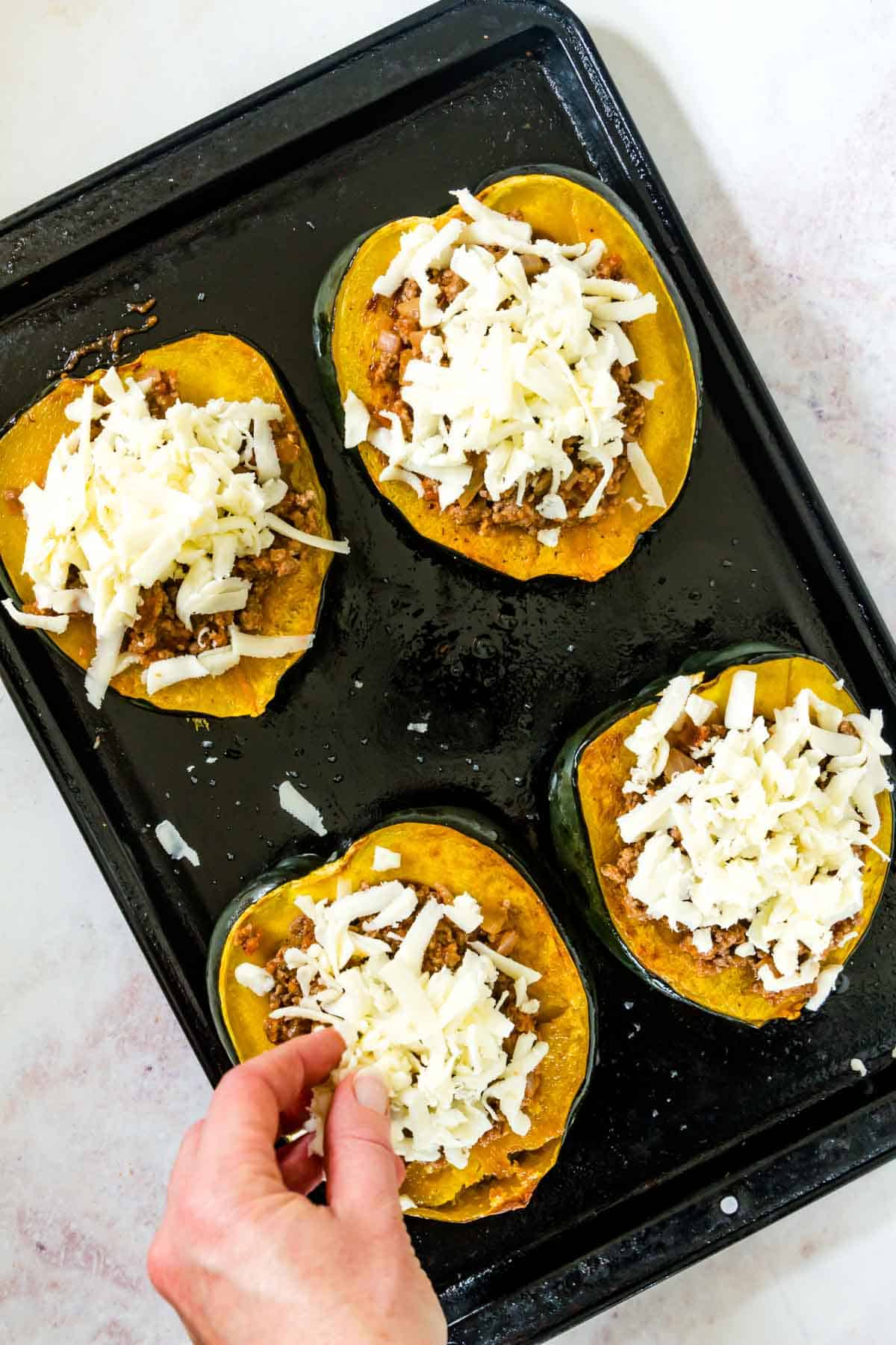 Mozzarella cheese being sprinkled over the stuffed acorn squash halves on a sheet pan.