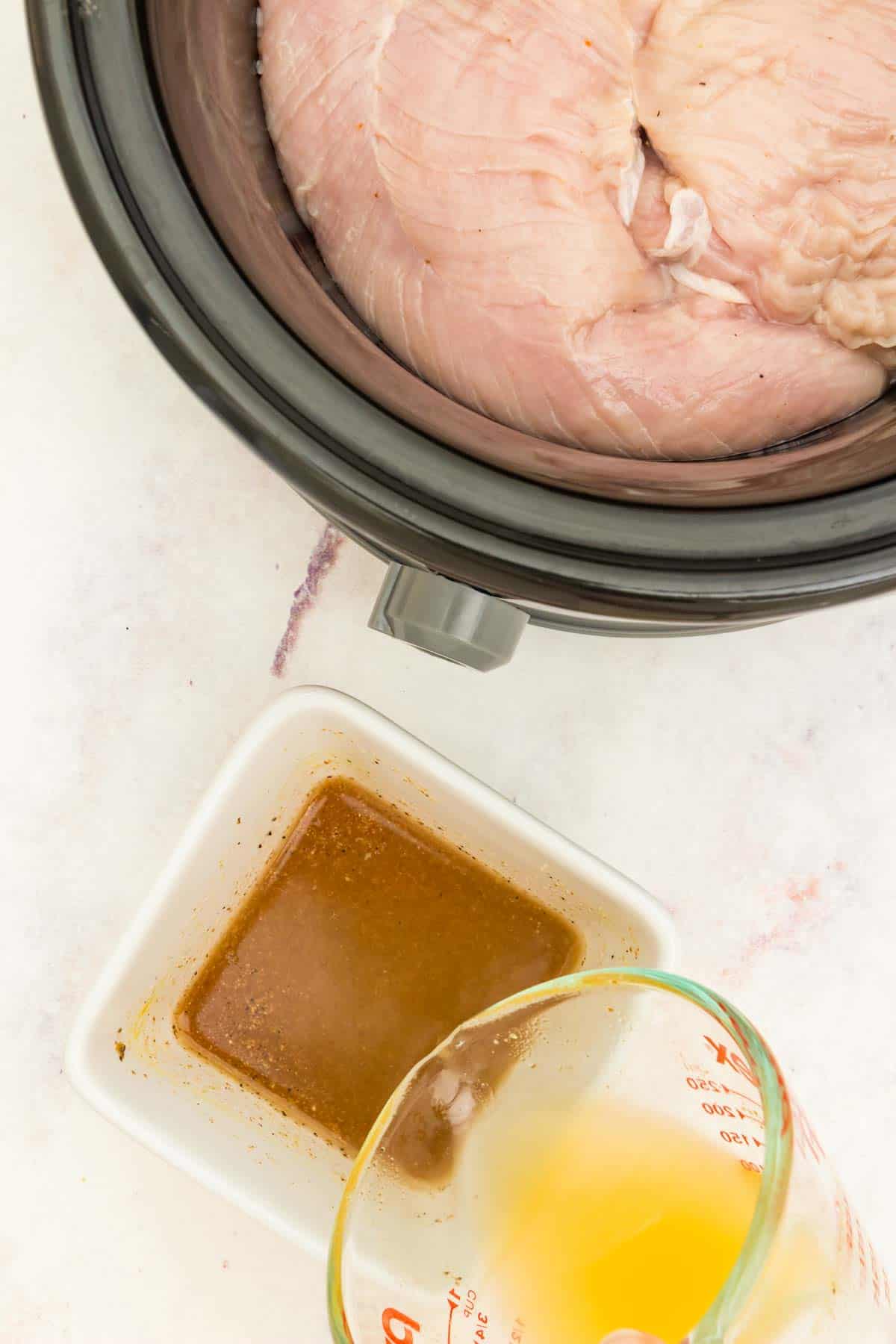 Chicken broth being poured into the bowl of sauce next to the crockpot with raw turkey tenderloins in it.