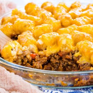 Sloppy Joe Tater Tot Casserole in a glass pie plate with one scoop removed so you can see the meaty filling.