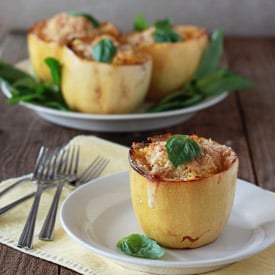 A cheesy stuffed spaghetti squash half with three more on a serving dish behind it.