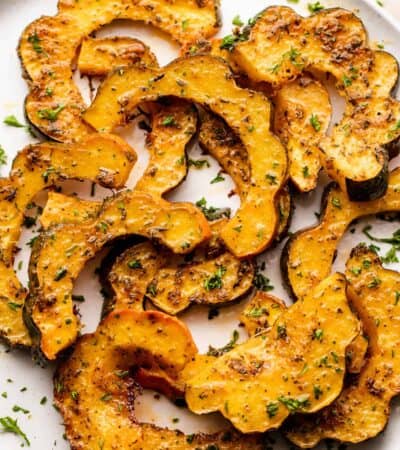 Pieces of roasted acorn squash on a platter garnished with herbs.