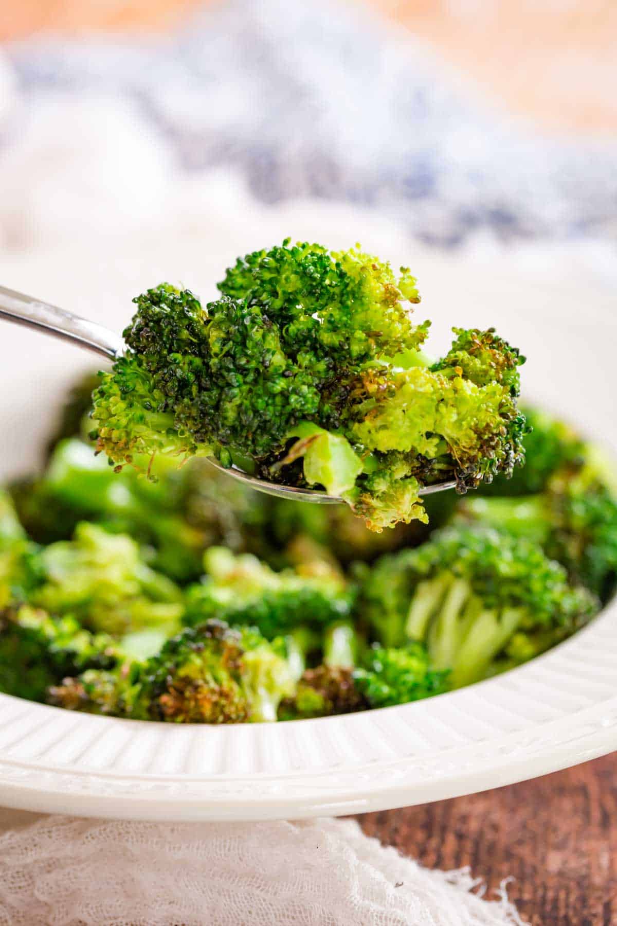 A spoonful of air fryer broccoli with a bowl of broccoli in the background.