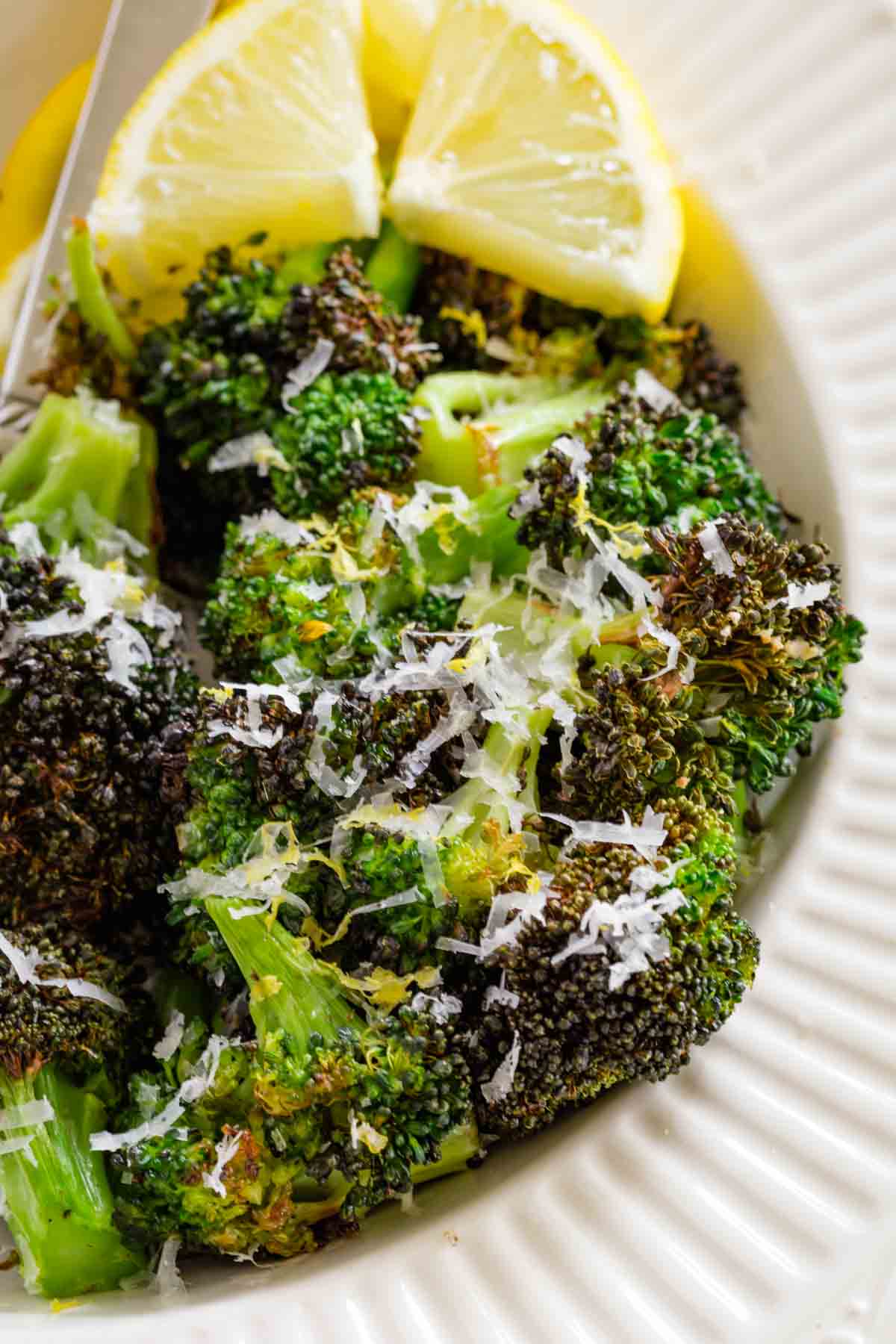 Air fryer broccoli in a bowl topped with grated parmesan next to two lemon wedges.