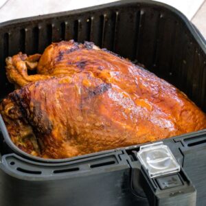 A golden brown bone-in turkey breast in an air fryer basket.