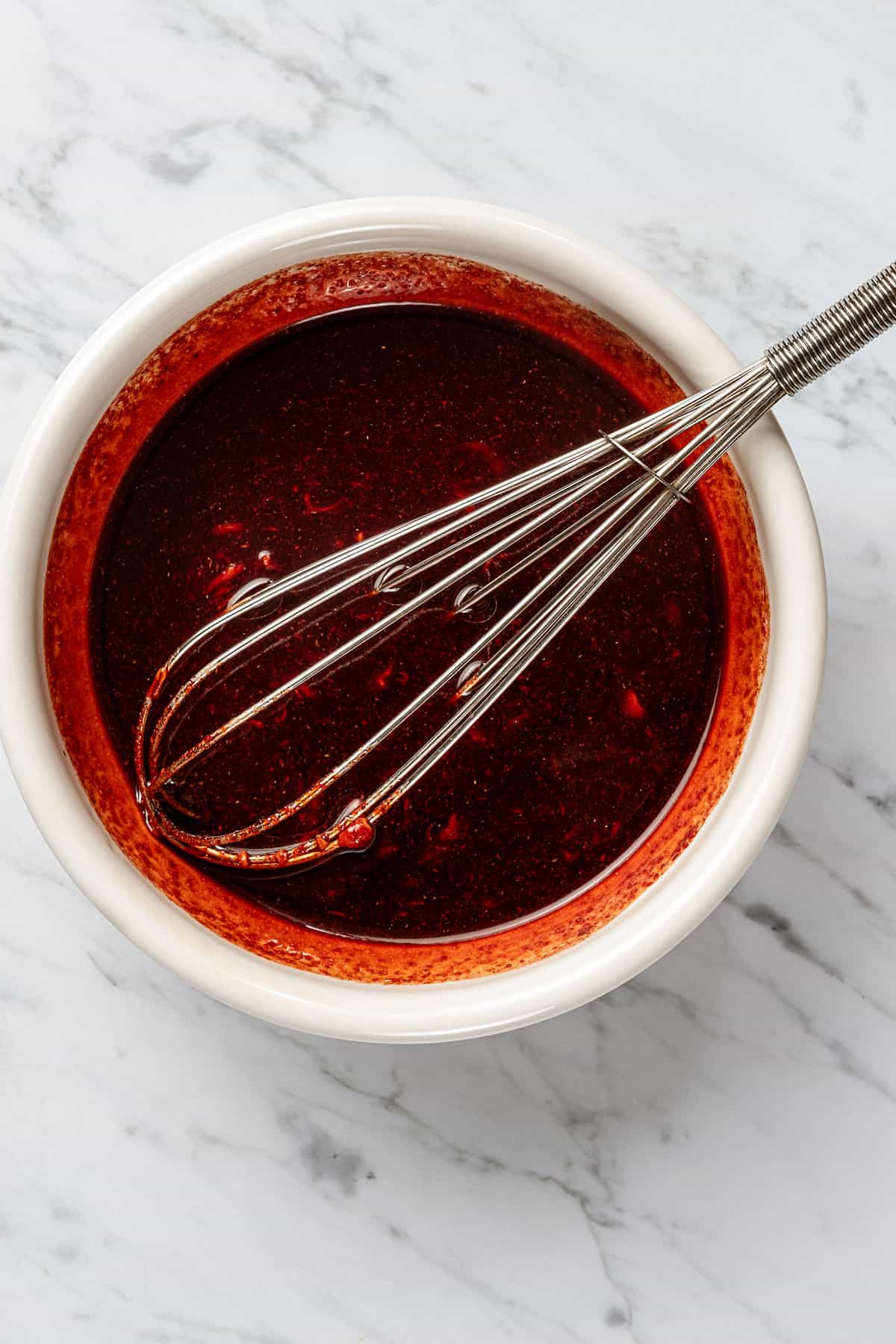 The marinade for char siu pork in a white bowl with a whisk.