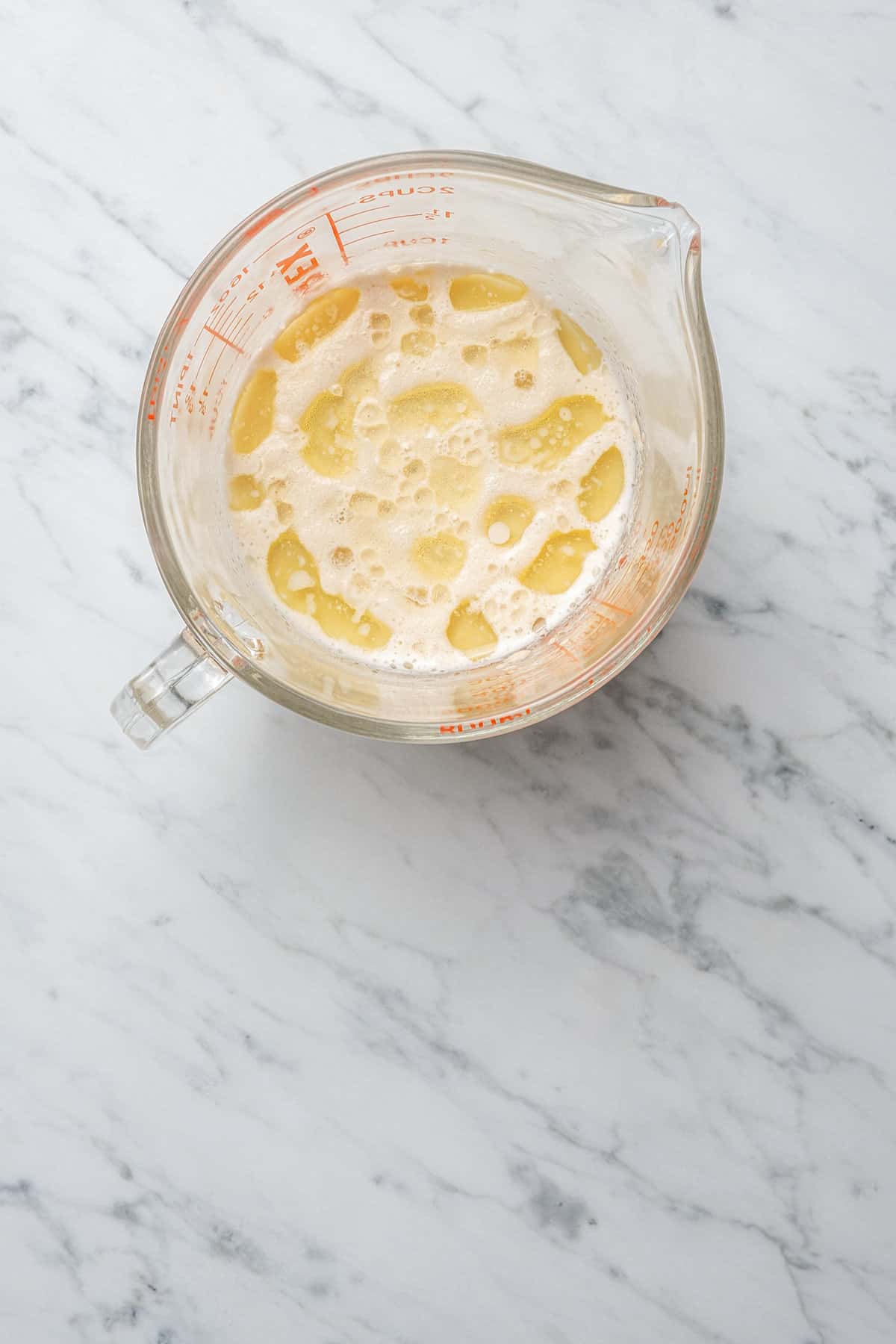 Milk combined with yeast and melted butter in a glass measuring cup.