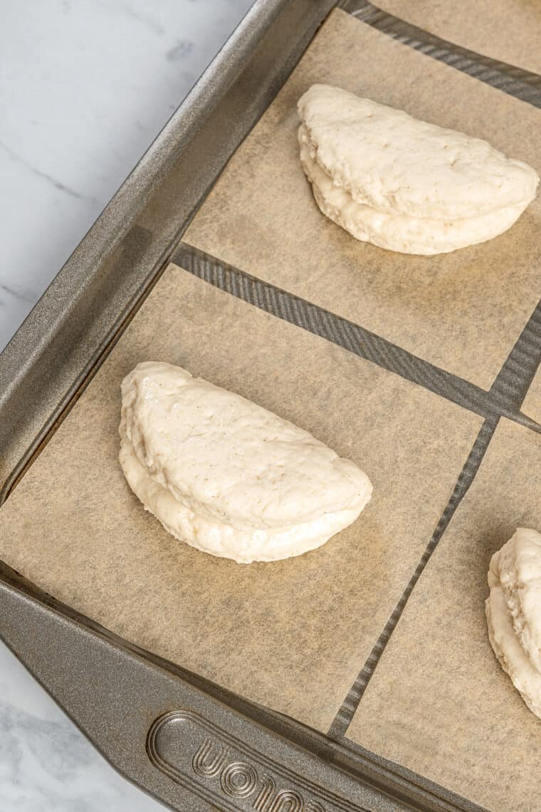 Close up of folded uncooked bao buns on squares of parchment paper on a baking sheet.