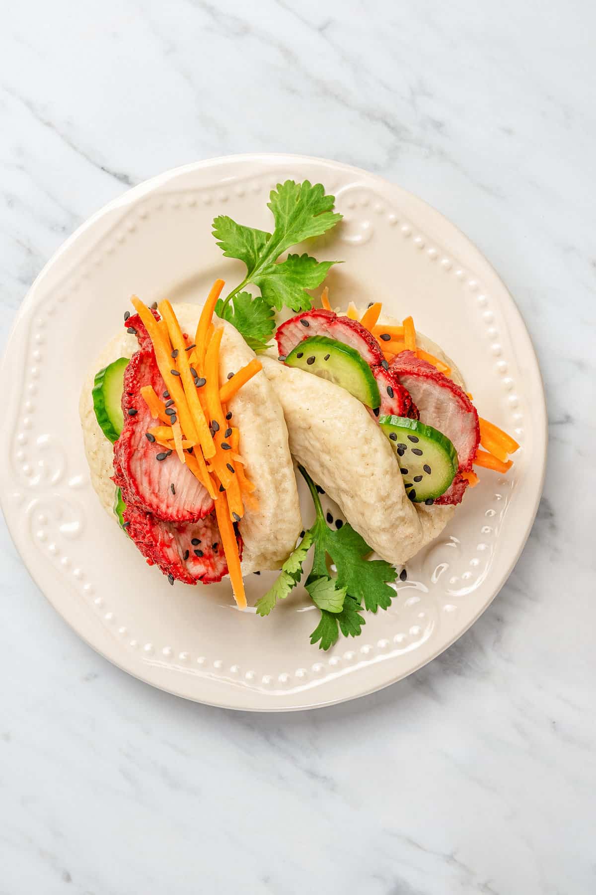 Overhead view of two gluten-free bao buns filled with char siu pork and veggies on a plate.