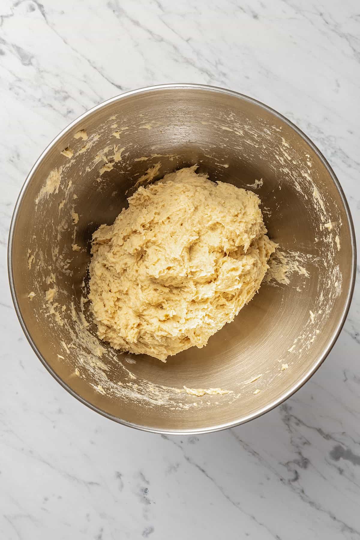 Wet and dry gluten-free bread ingredients combined into a dough inside a metal mixing bowl.