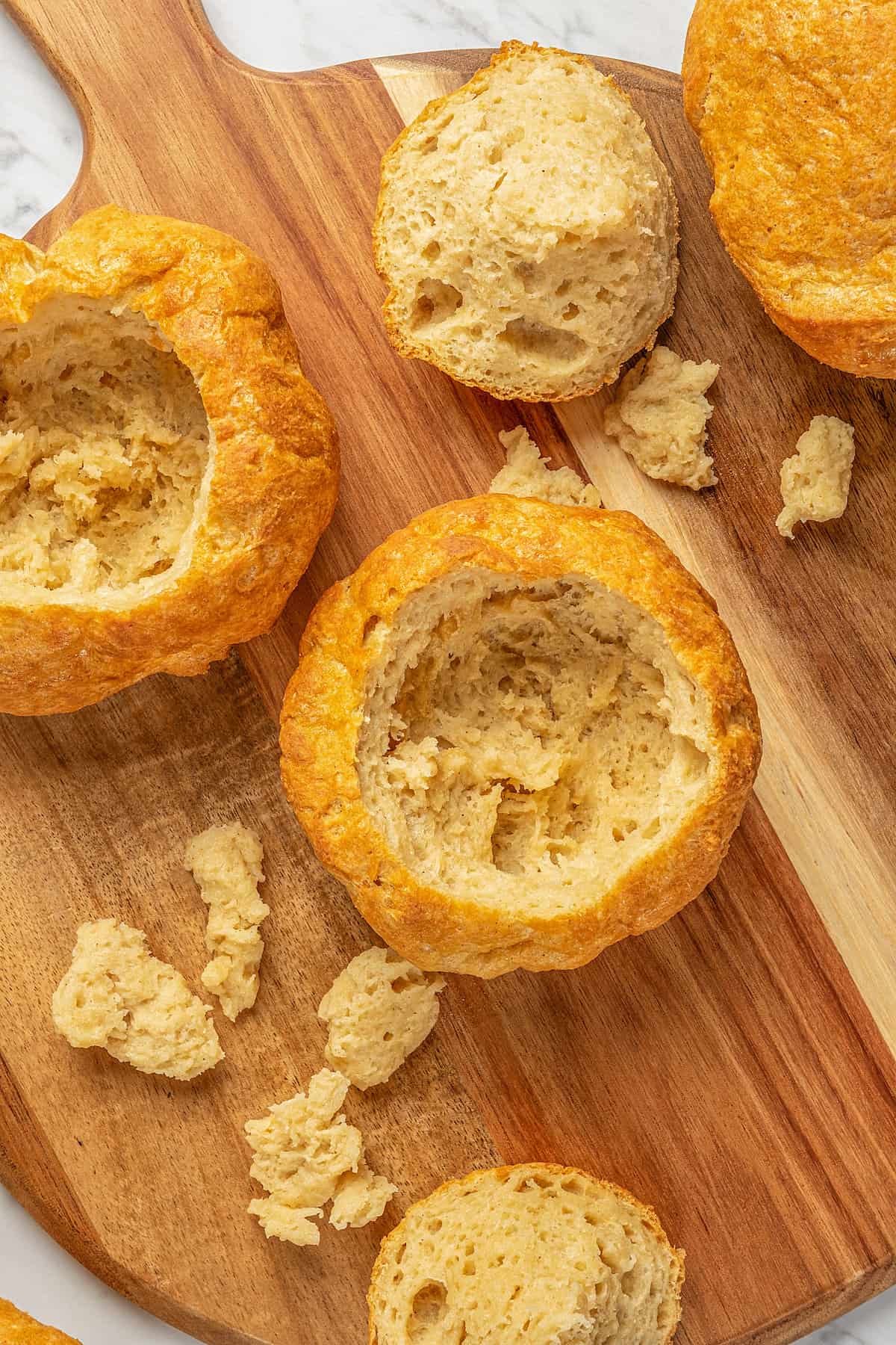 Overhead view of two gluten-free bread bowls carved out on a wooden cutting board.