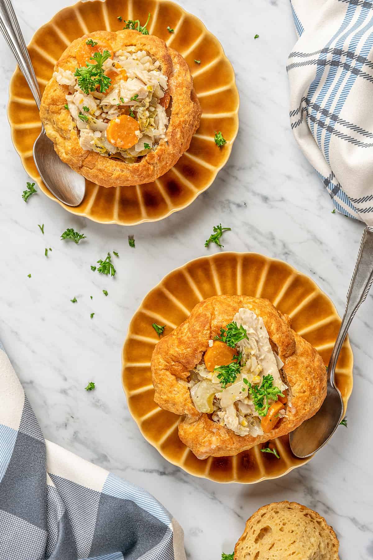 Overhead view of two gluten-free bread bowls on brown plates, filled with chicken and vegetables.