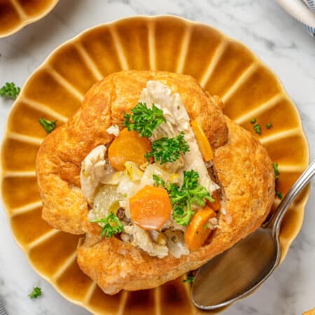 Overhead close up of a gluten-free bread bowl on brown plates, filled with chicken and vegetables.