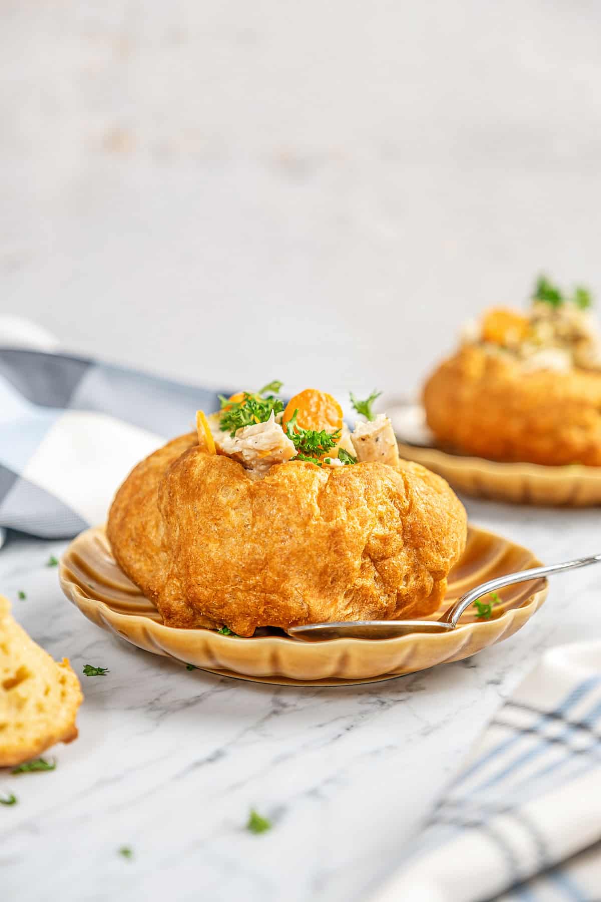 A gluten-free bread bowl on a plate filled with chicken and vegetables.