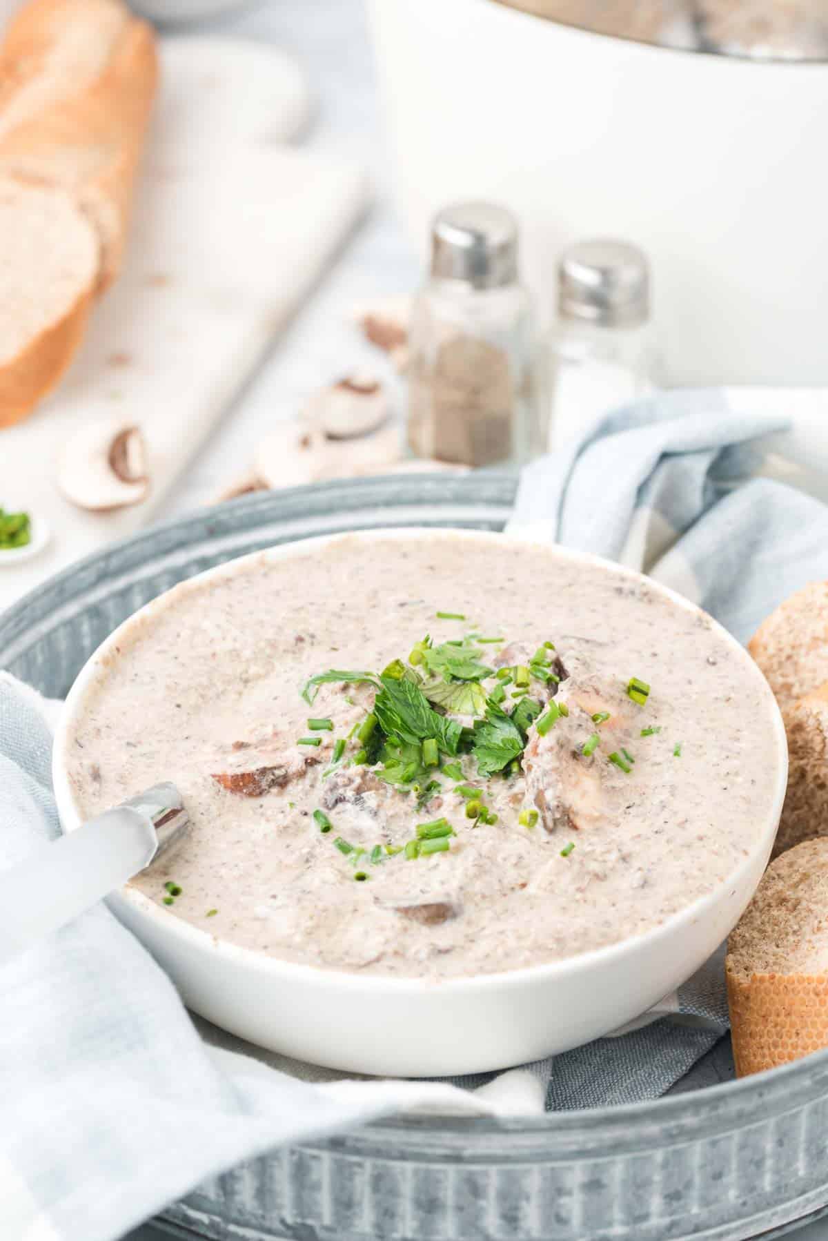 A bowl of cream of mushroom soup garnished with fresh parsley, next to slices of crusty bread.