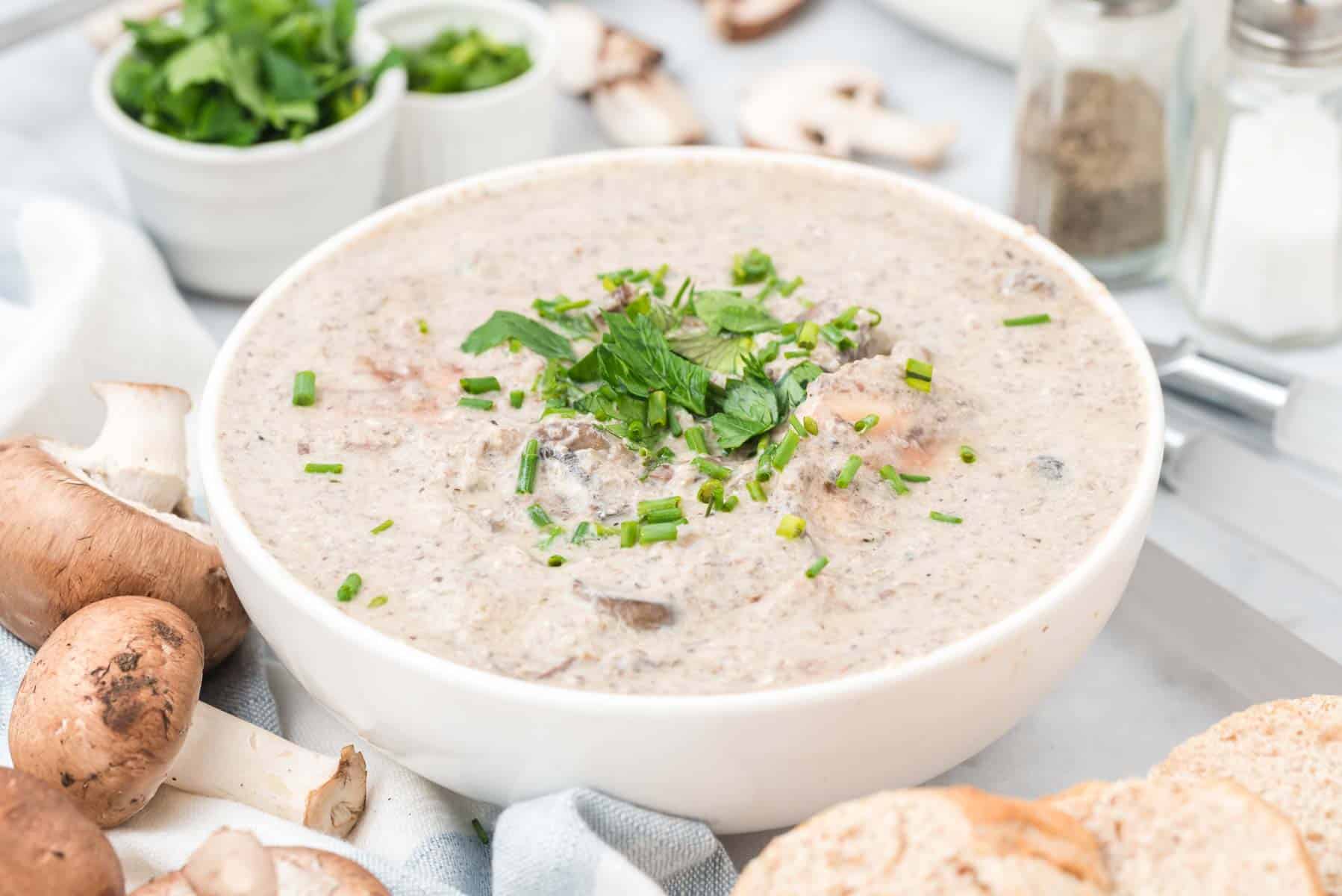 A bowl of cream of mushroom soup garnished with fresh parsley, surrounded by mushroom soup ingredients.
