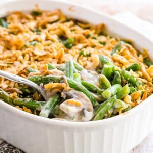 A spoon picking up a scoop of gluten free green bean casserole from a white baking dish.