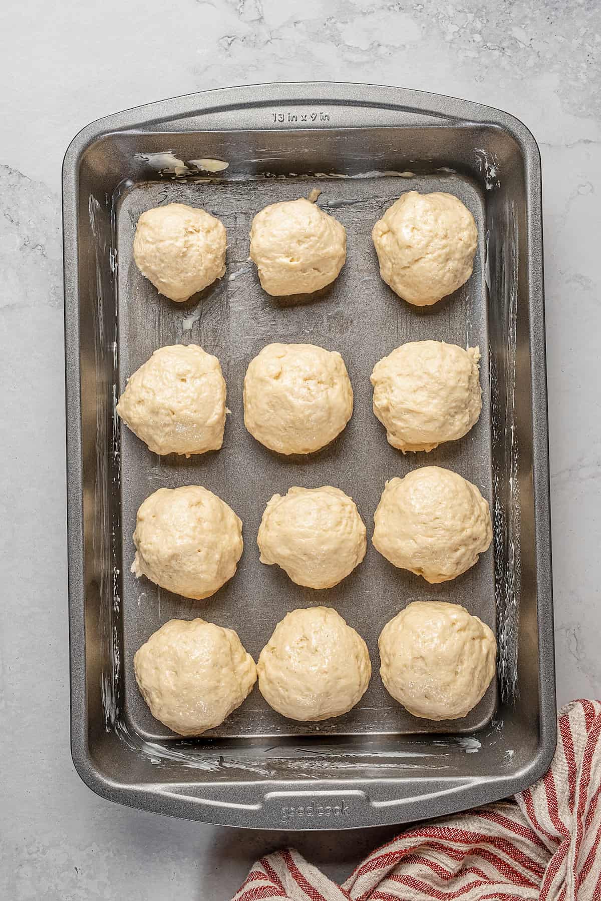 A dozen dough balls arranged in rows on a baking sheet.