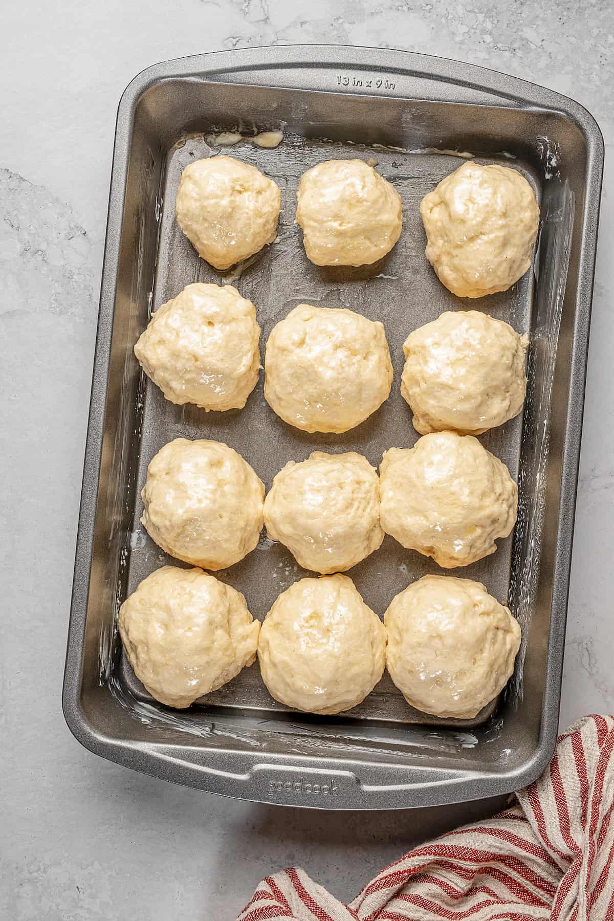 A dozen dough balls arranged in rows on a baking sheet.