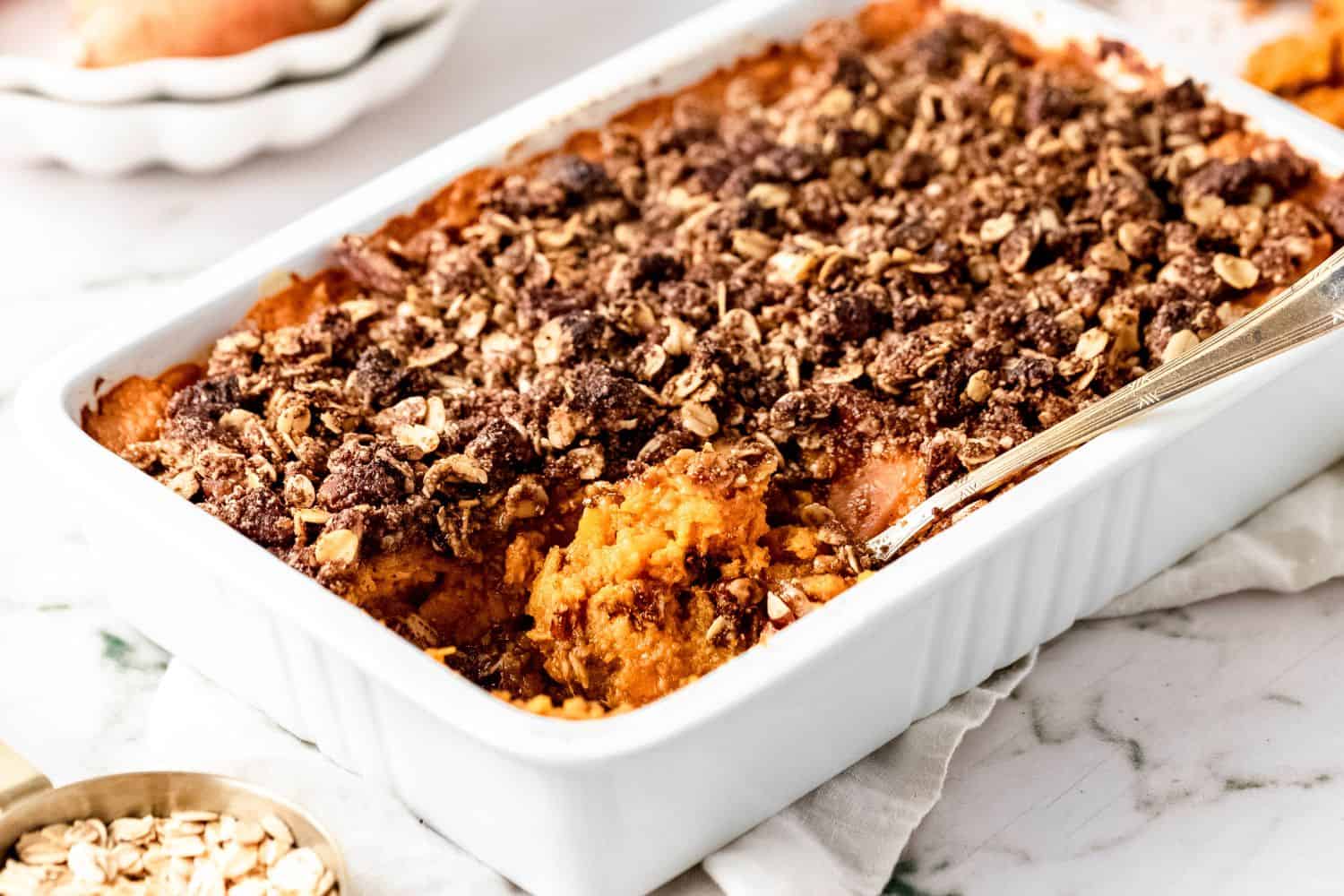 A spoon with a scoop of sweet potato casserole on it in a white ceramic baking dish.