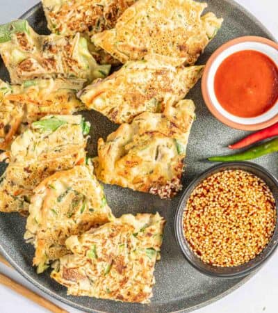 Vegetable pancake wedges arranged on a plate with spicy Korean dipping sauces.
