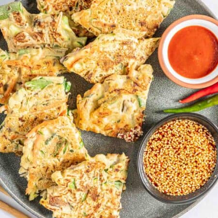 Vegetable pancake wedges arranged on a plate with spicy Korean dipping sauces.