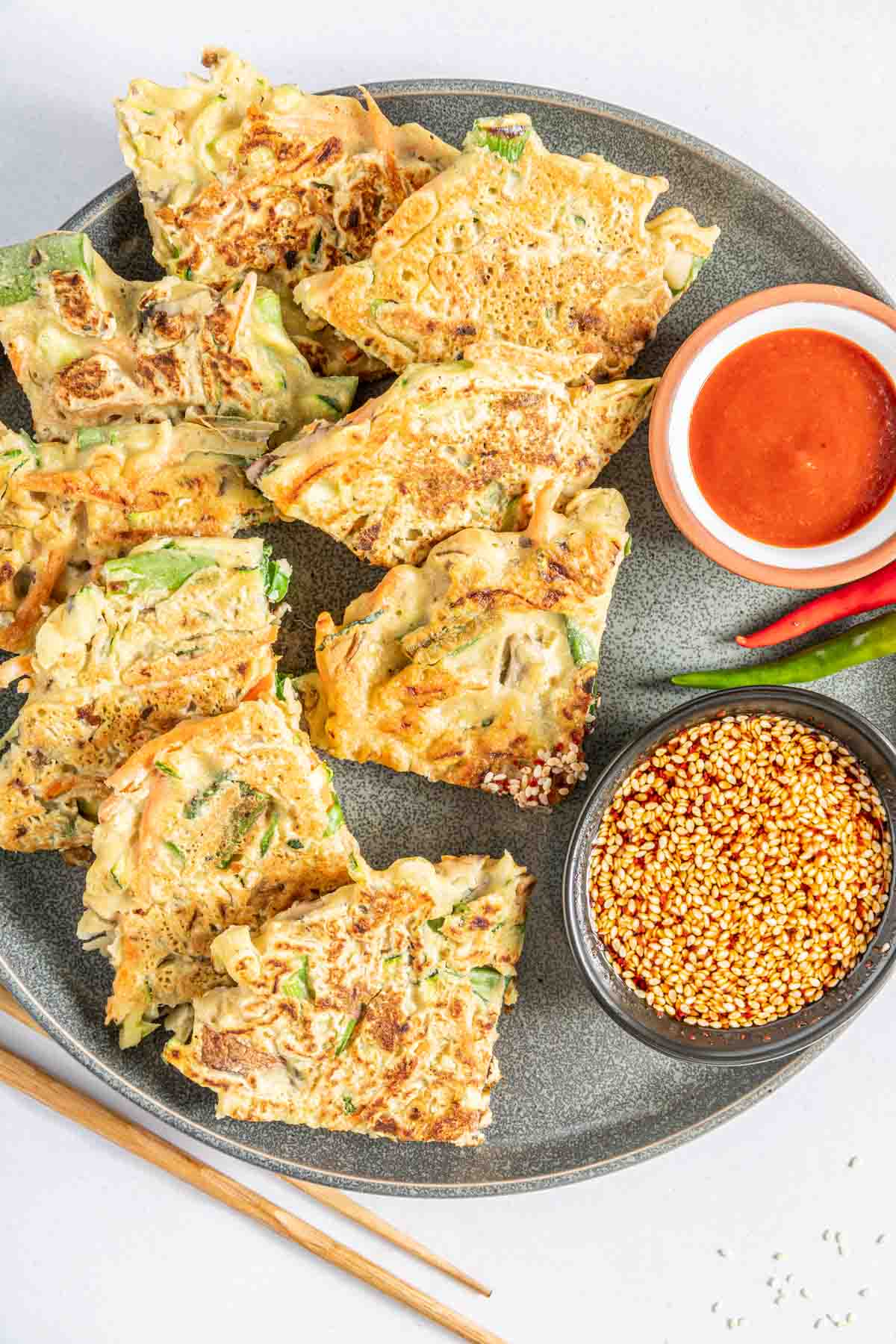 Vegetable pancake wedges arranged on a plate with spicy Korean dipping sauces.