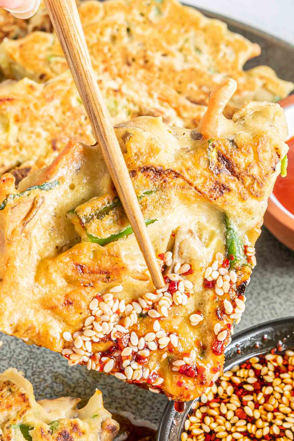 Chopsticks holding a vegetable pancake dipped in Korean dipping sauce.