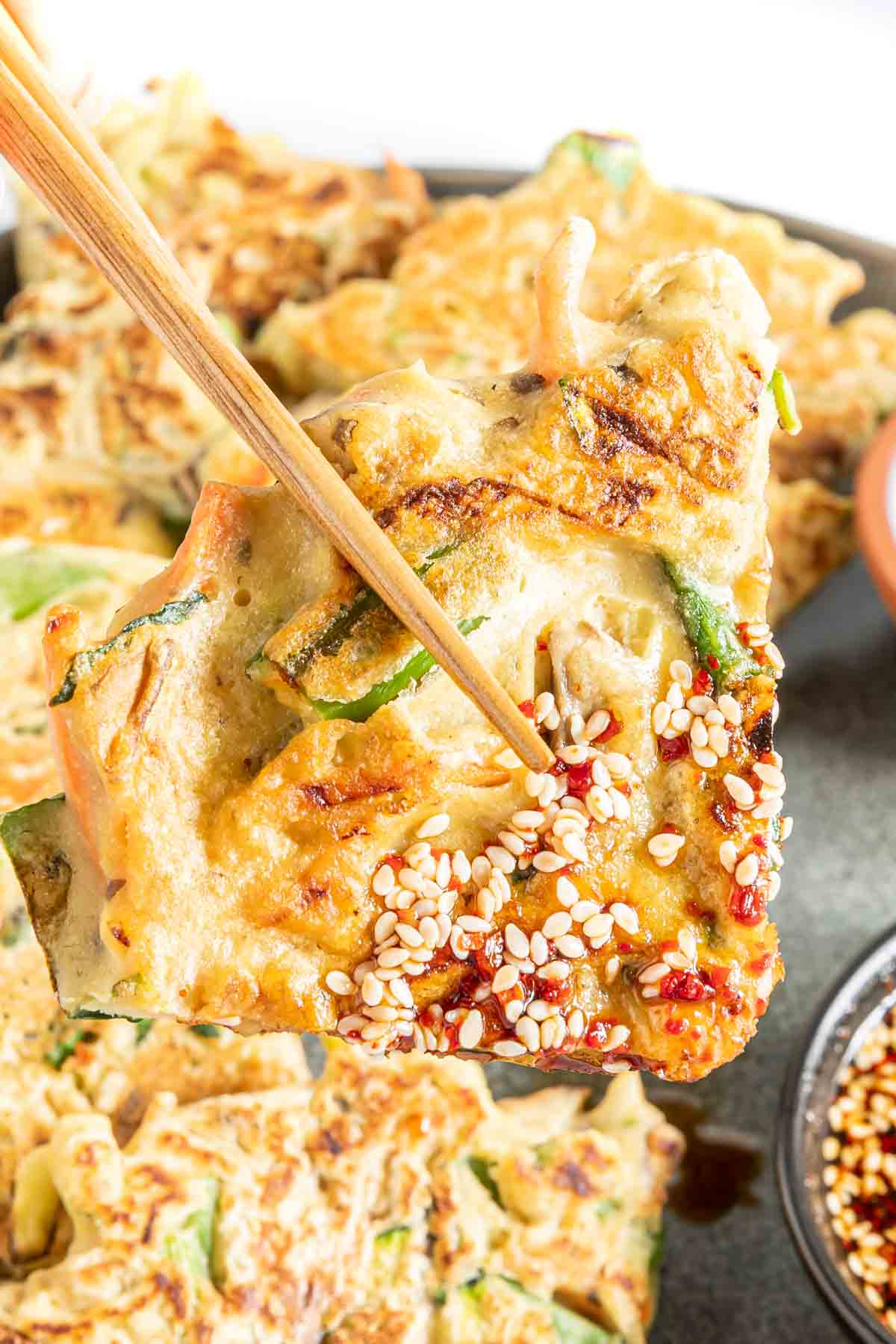 Chopsticks holding a vegetable pancake dipped in Korean dipping sauce.