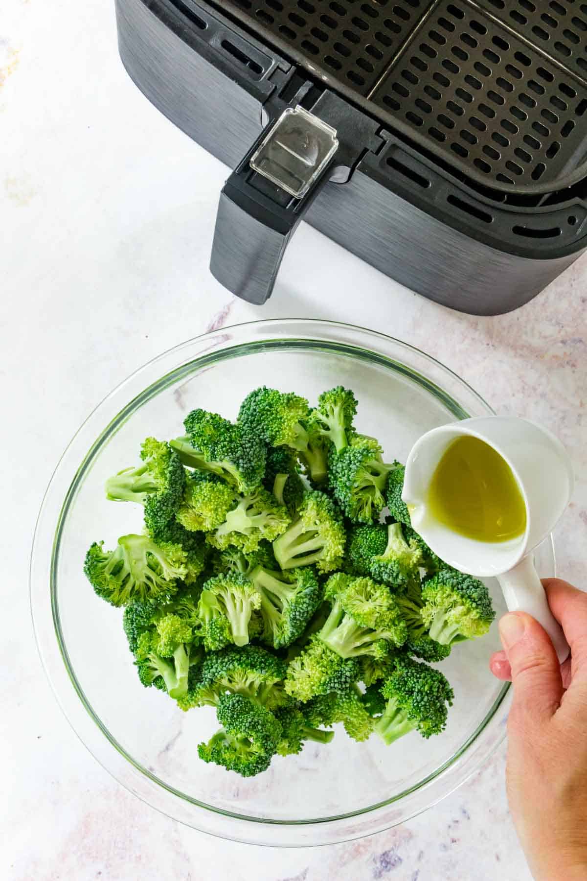 Olive oil is added to a bowl of broccoli florets.