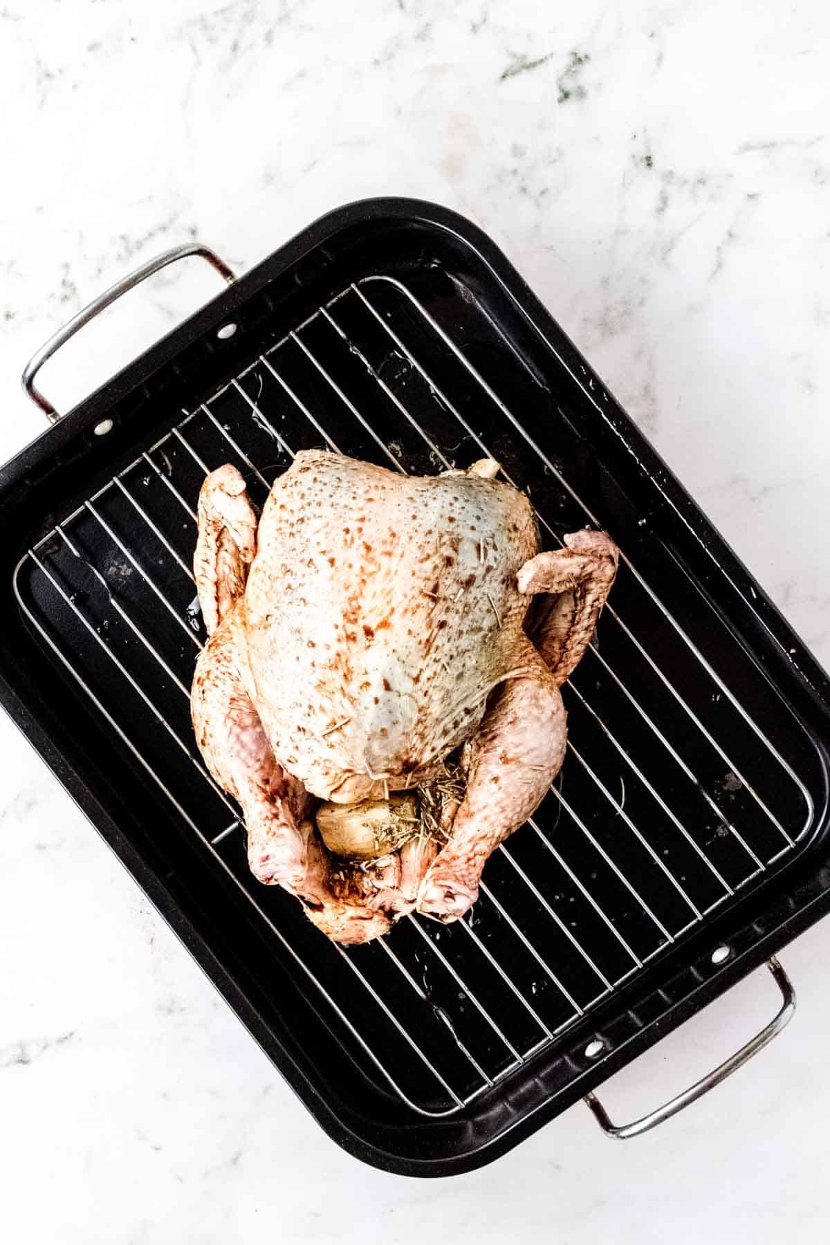 Overhead view of a whole raw chicken in a roasting pan, stuffed with onion and rubbed with rosemary balsamic marinade.