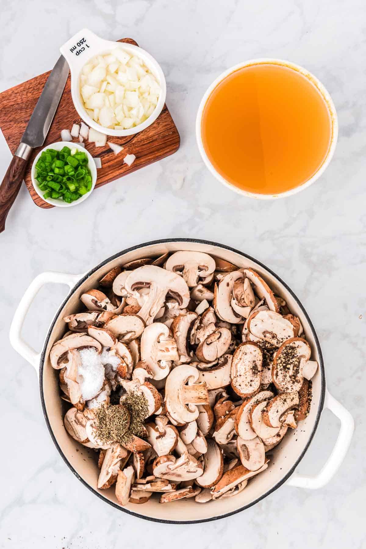 Mushrooms in a large pot next to bowls of broth and garnishes.