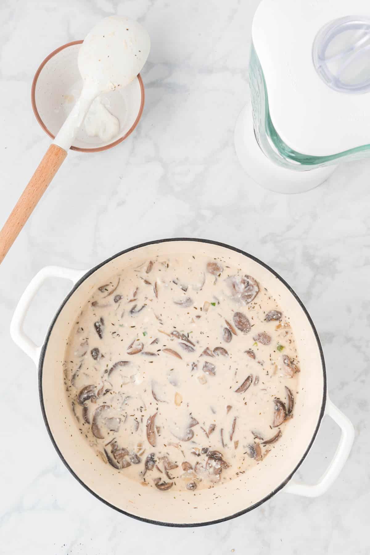 A pot of cream of mushroom soup next to a stirring spoon and a blender.