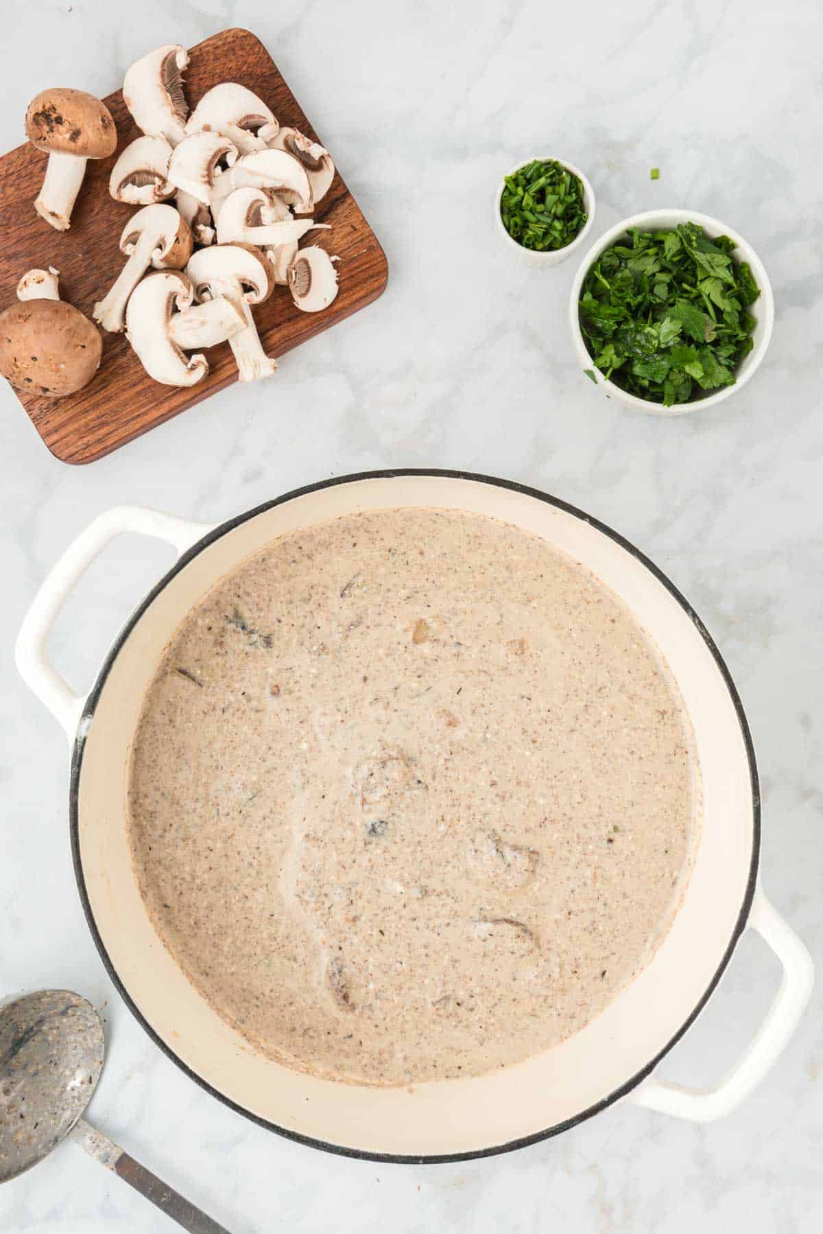 Healthy cream of mushroom soup in a large pot next to small bowls of garnishes and chopped mushrooms.