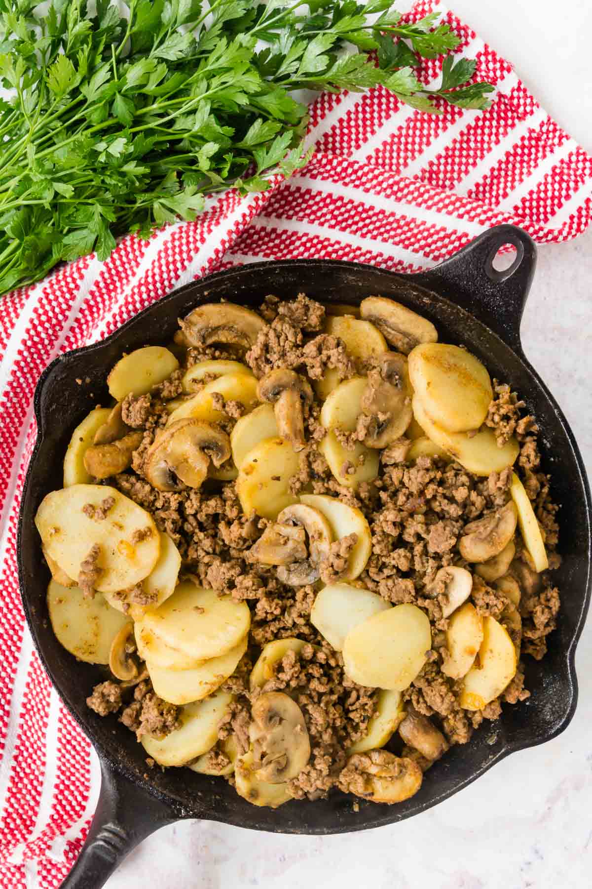 Cooked ground beef with sliced potatoes and mushrooms in a cast iron pan.