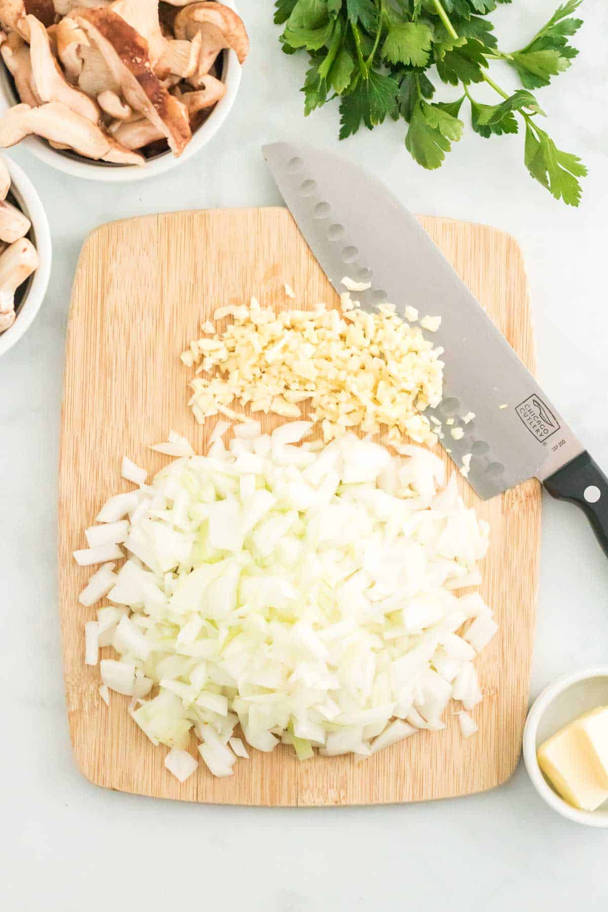 Diced onions on a wooden cutting board next to a large knife.