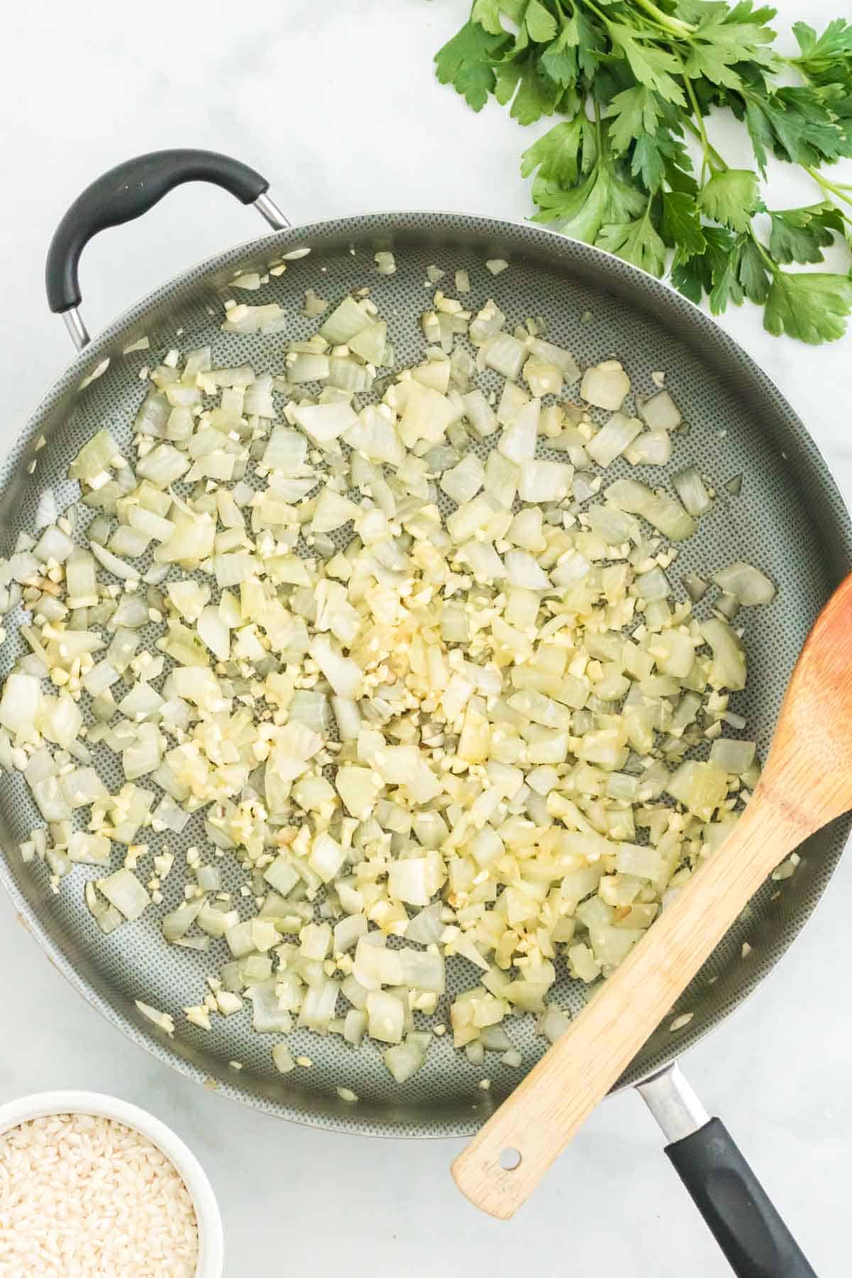 Diced and sauteed onions in a skillet next to a wooden spoon.