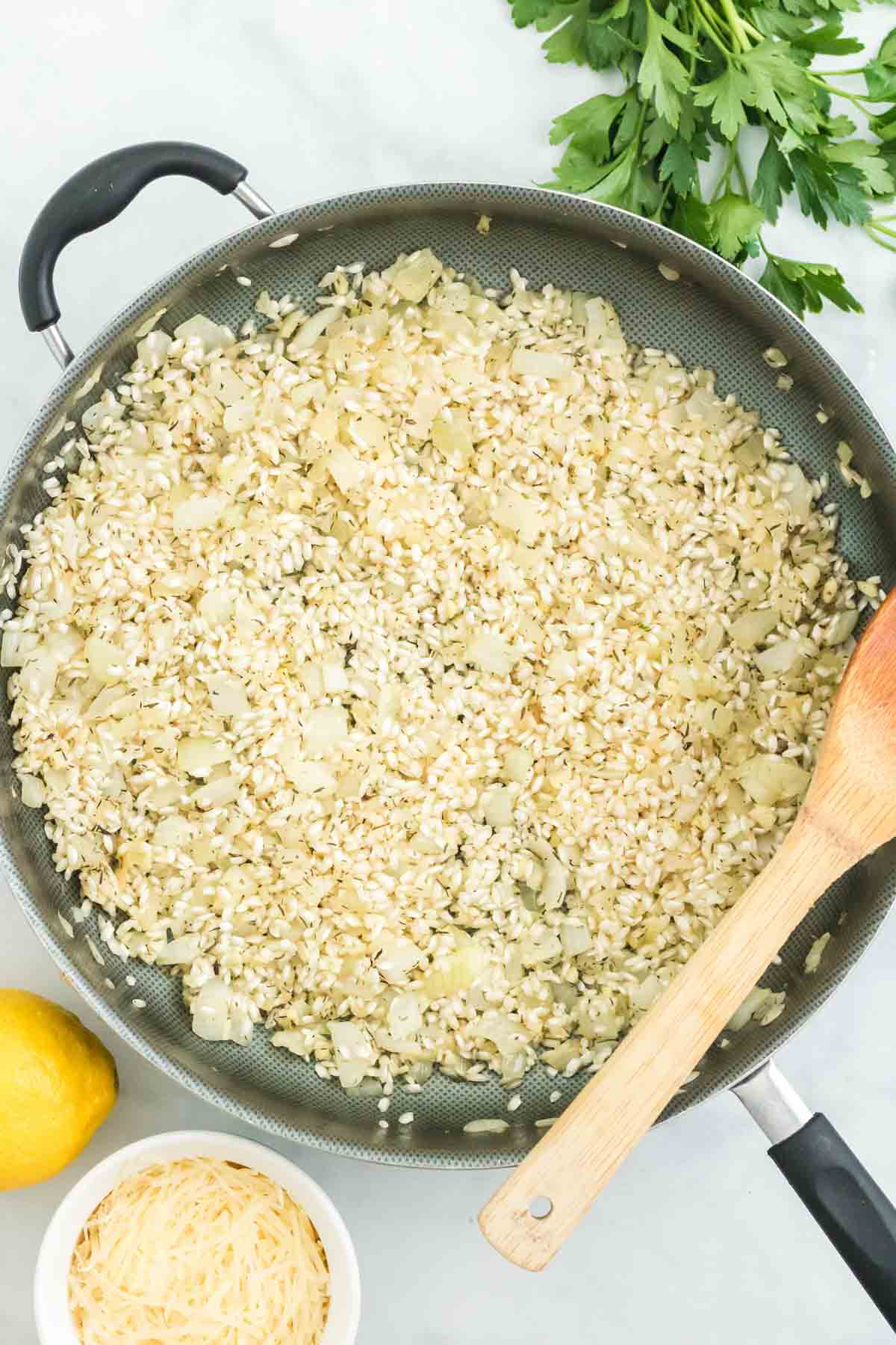 Arborio rice added to a skillet with sauteed onions.