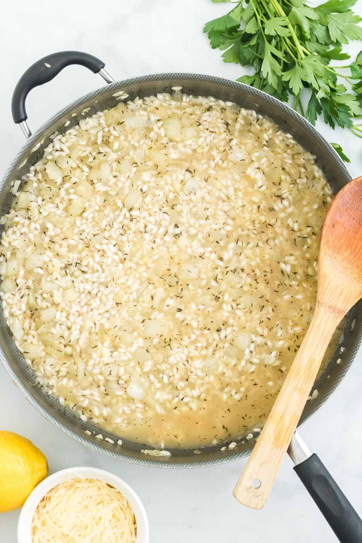 Broth is added to a skillet with arborio rice and sauteed onions.