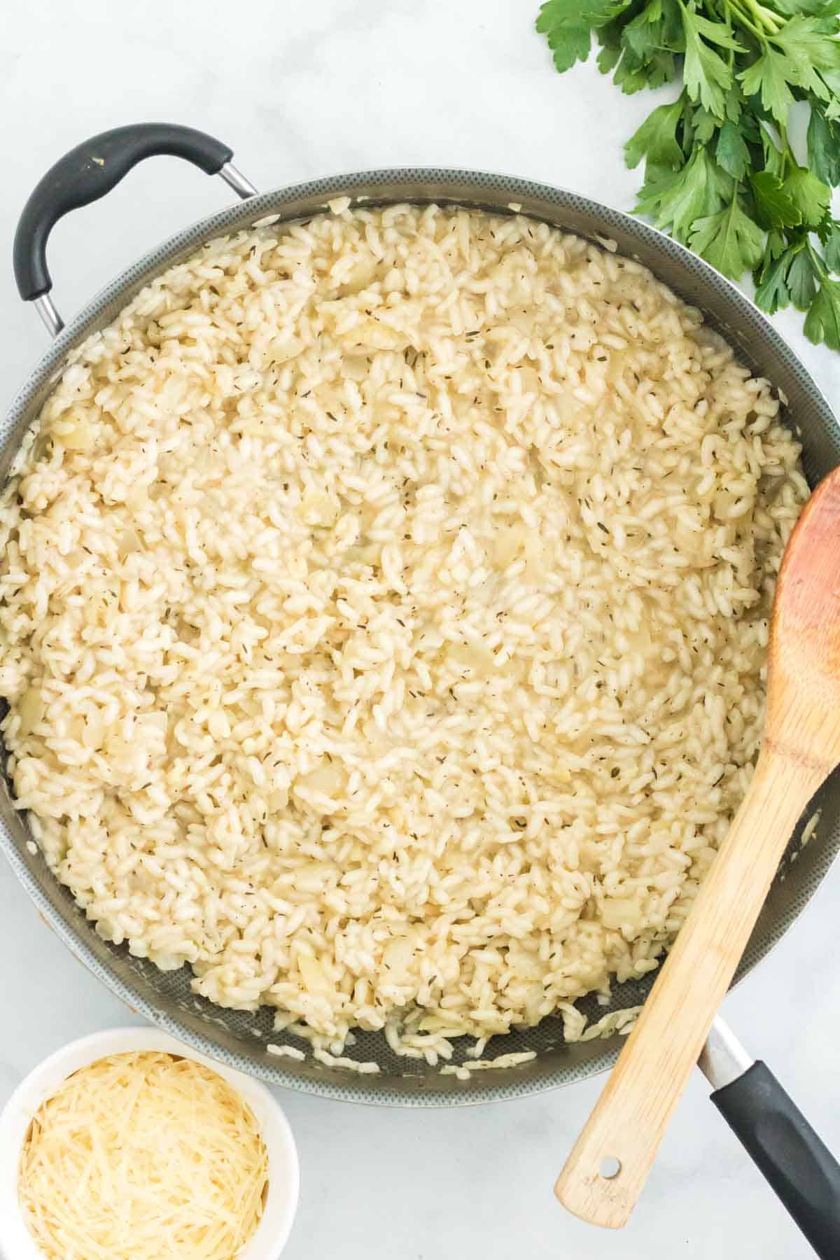 Cooked risotto in a skillet next to a wooden spoon.