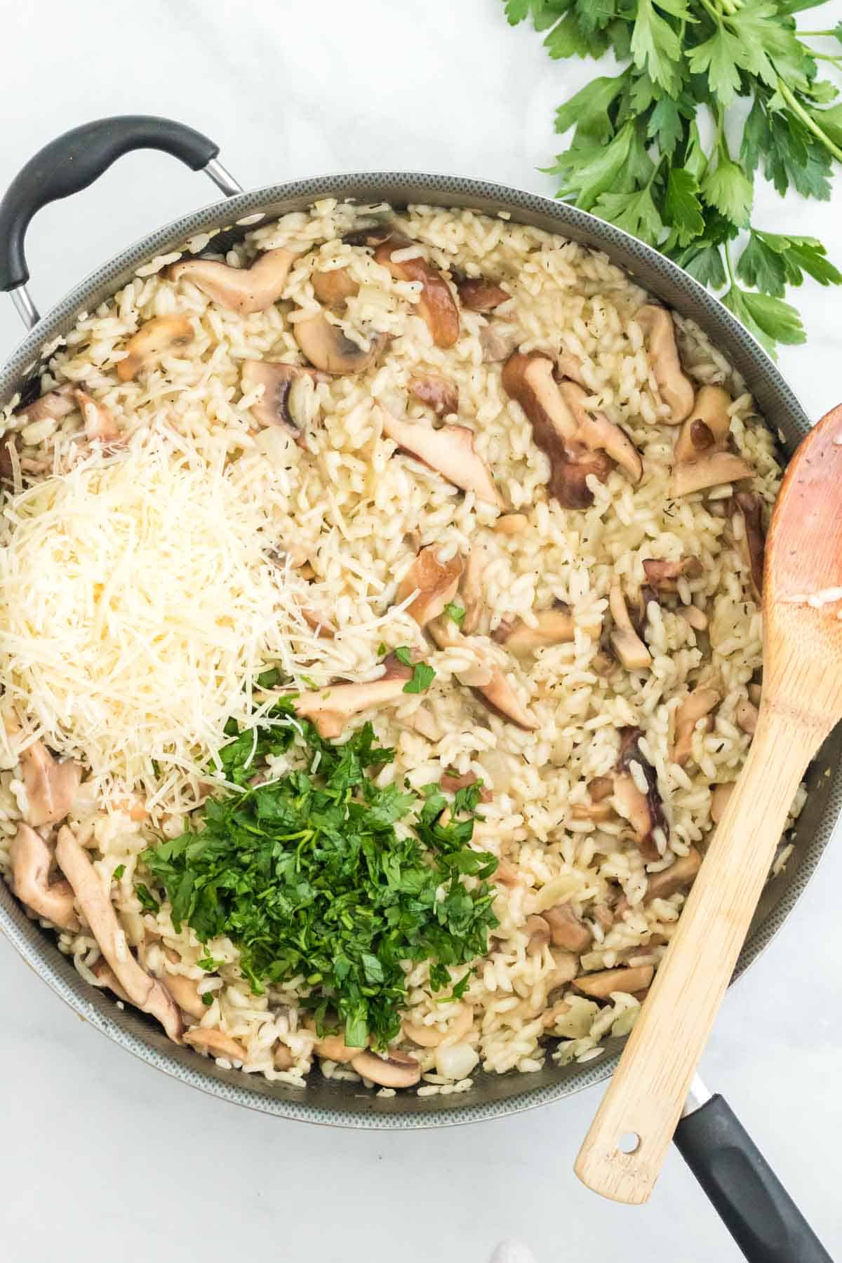 Sauteed mushrooms, parsley, and parmesan cheese added to risotto in a skillet.
