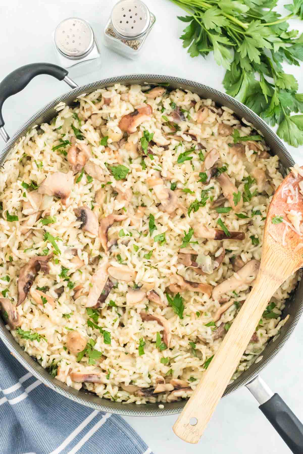 Finished mushroom risotto in a skillet next to a wooden spoon.