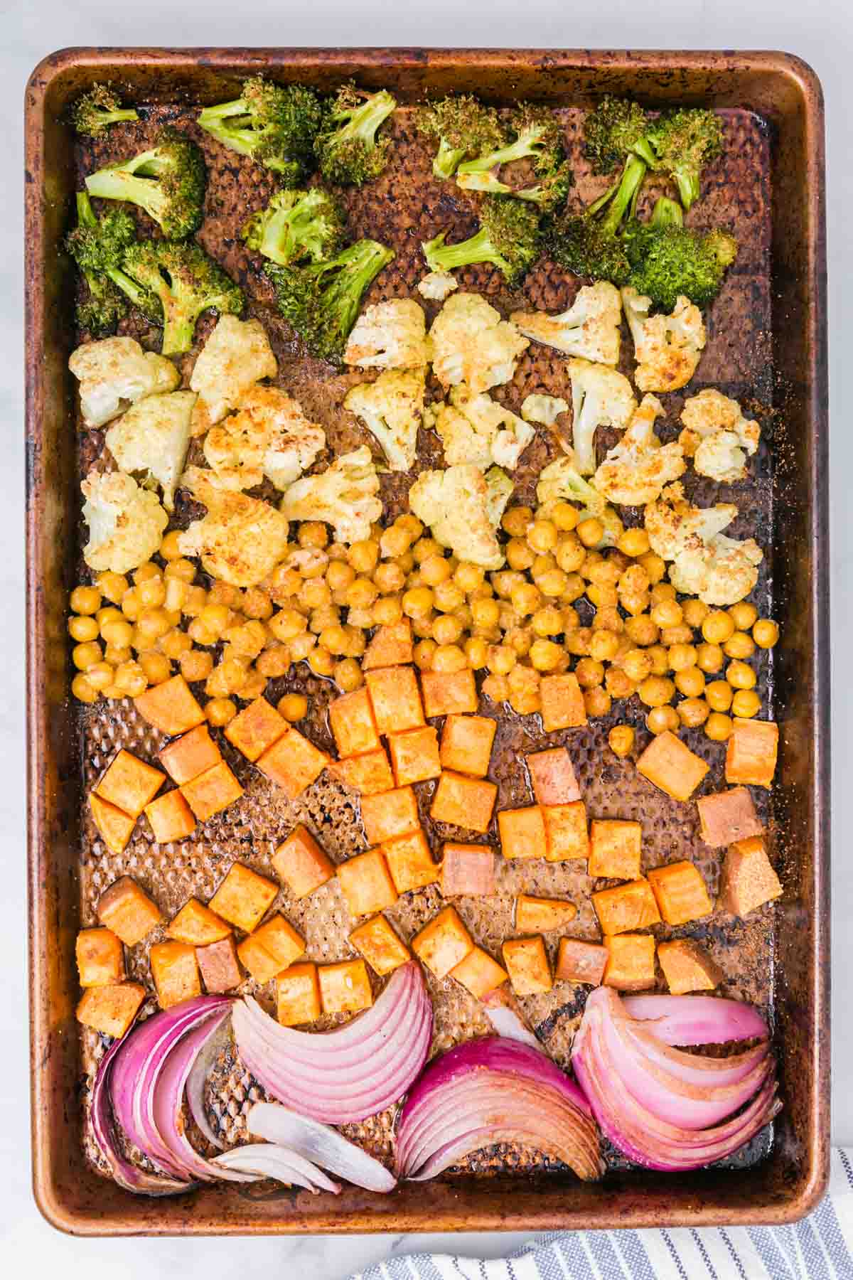 Assorted seasoned and roasted vegetables on a sheet pan.