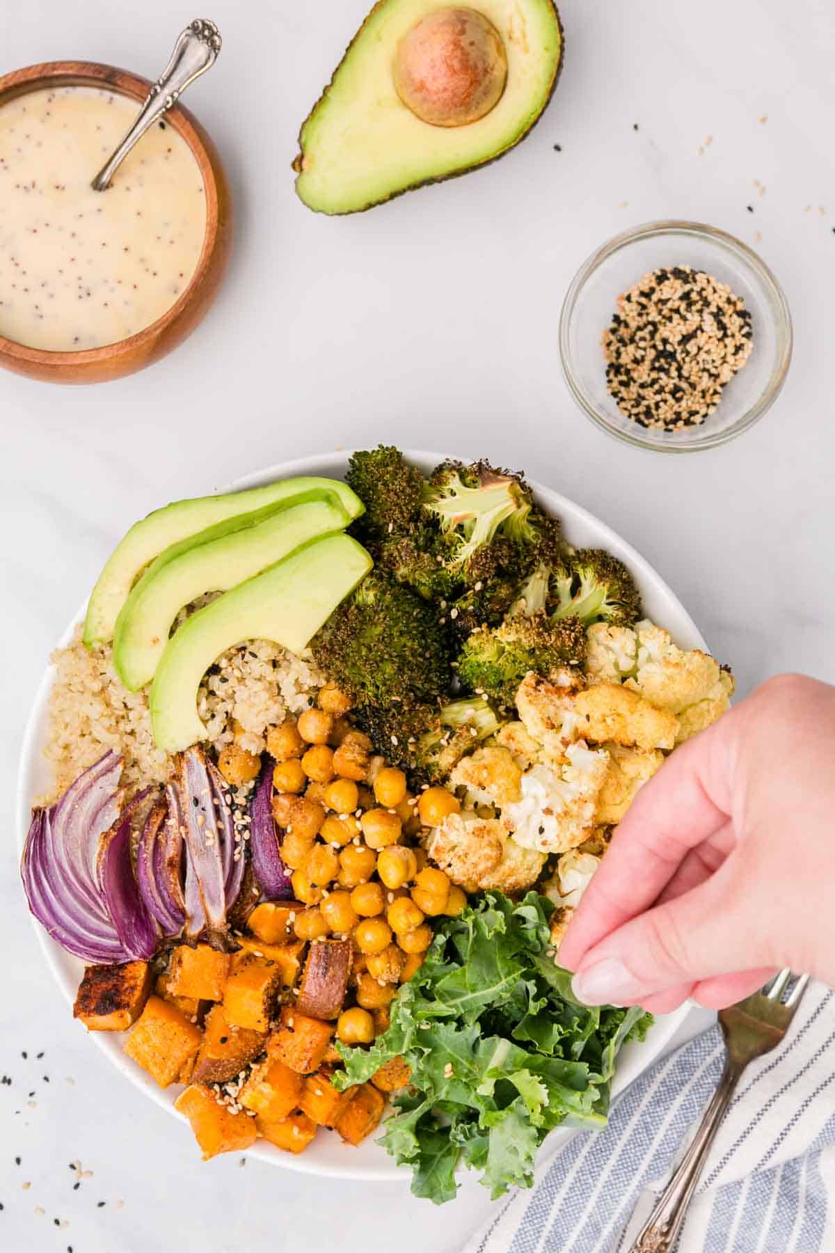 A hand sprinkles seasoning over top of an assembled buddha bowl.