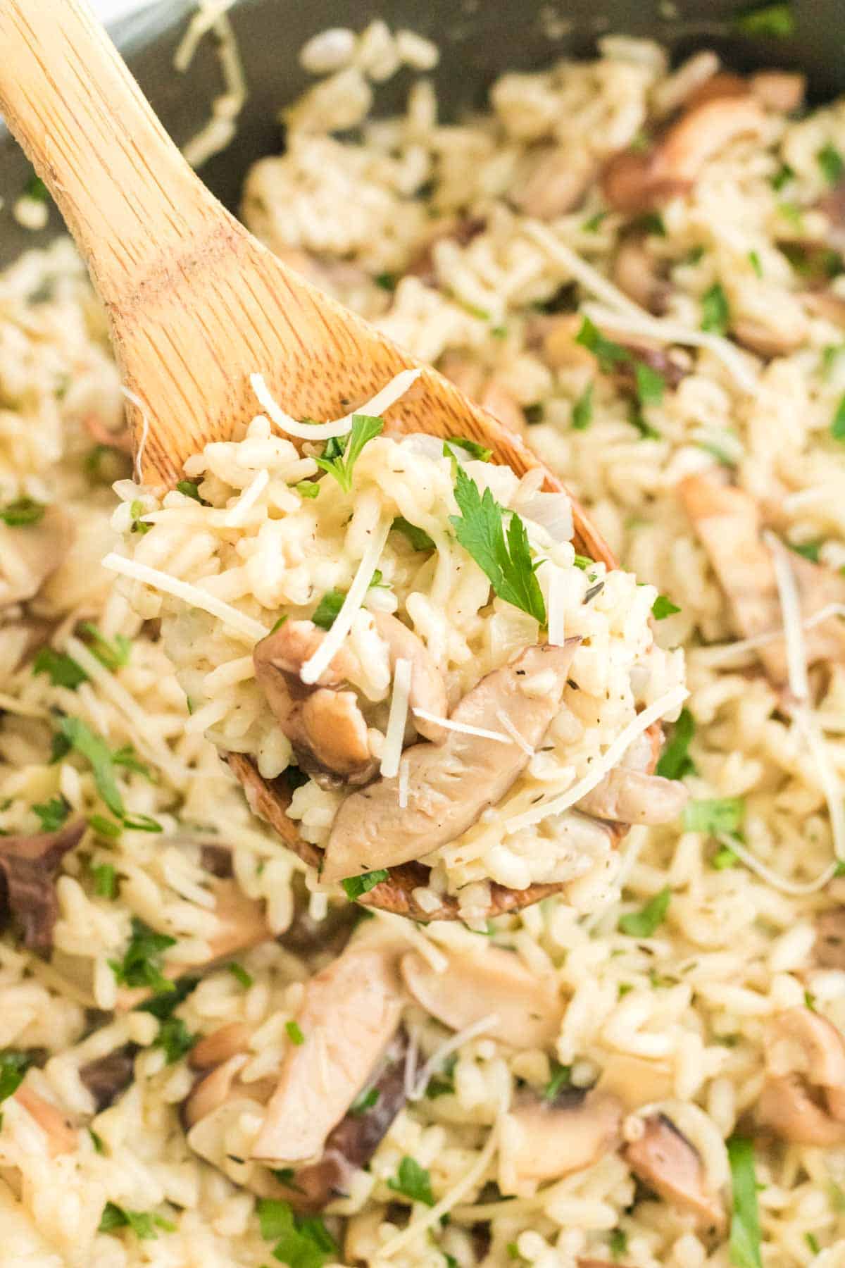 A wooden spoon stirs mushroom risotto in a skillet.