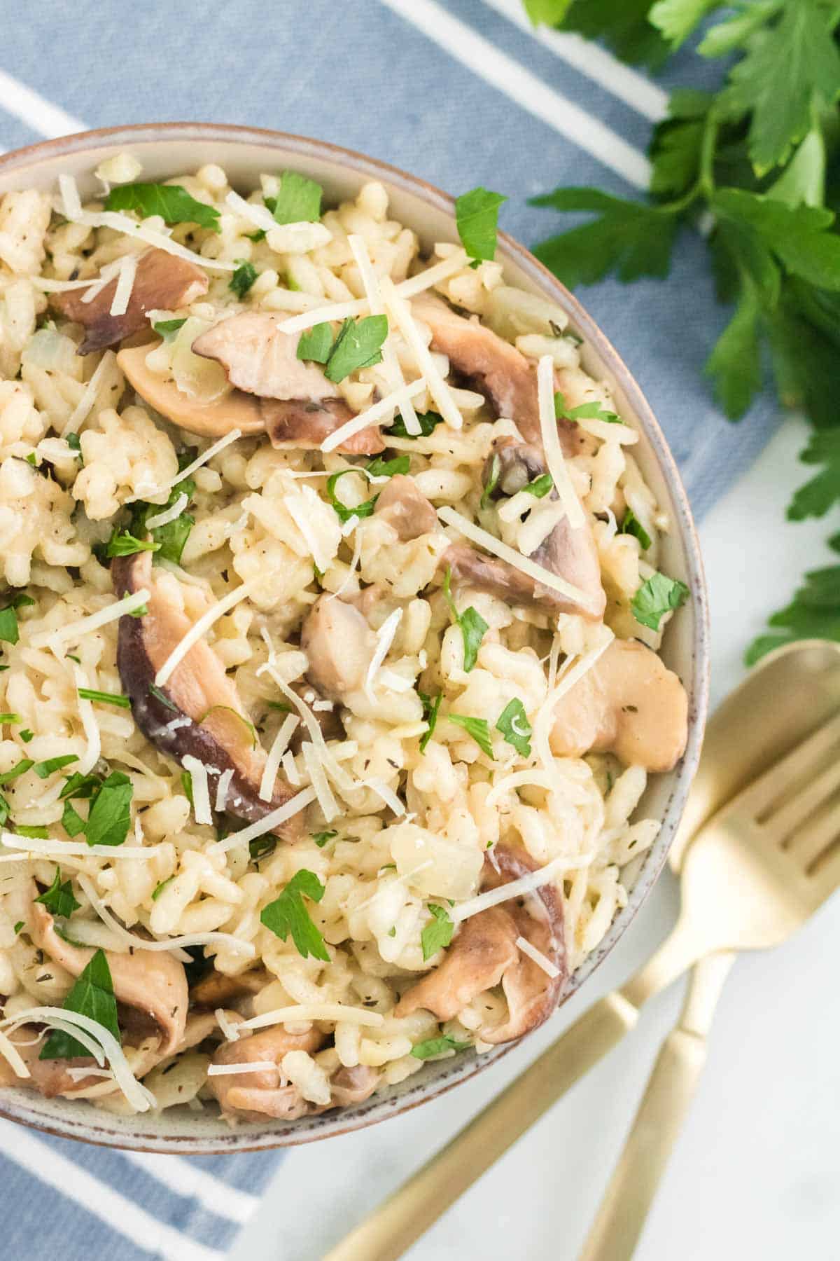 Close up of a bowl of mushroom risotto next to a fork and spoon.