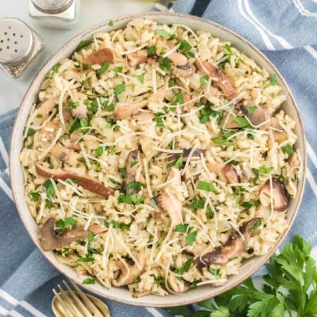 Overhead view of a bowl of mushroom risotto next to a fork and spoon, and lemon wedges on a blue table cloth.